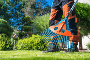 A gardener is holding a rake and other gardening tools